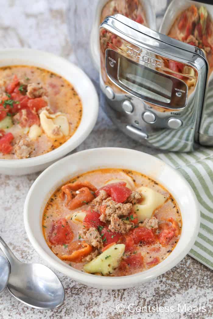 Creamy tomato tortellini soup in white bowls with a Crock-Pot in the background