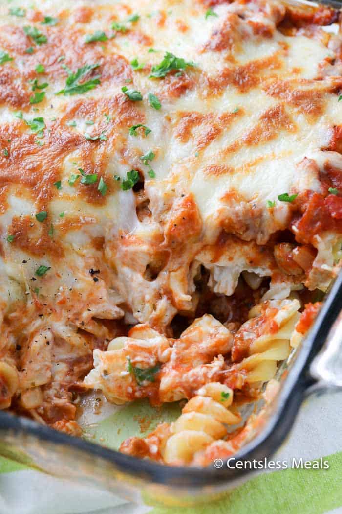 Sour cream noodle bake in a clear dish with a scoop taken out and parsley on top