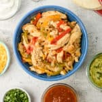 Crock-Pot chicken fajitas in a blue bowl with salsa guacamole cilantro cheese and sour cream on the side