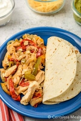 Crock-Pot chicken fajitas on a blue plate with sour cream cheese and Guacamole in the background