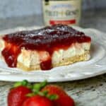 Strawberry cheesecake bar on a white plate with strawberries and jam in the background