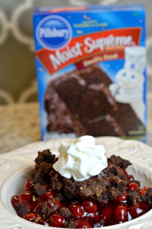 Chocolate cherry dump cake recipe in a bowl topped with whipped cream and Pillsbury black forest cake in the background