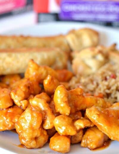 Easy orange chicken on a plate with rice and spring rolls