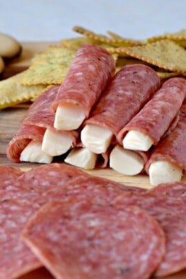 Meat cheese and crackers on a wooden board with some cheese wrapped in salami