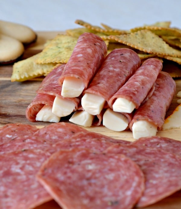 Meat cheese and crackers on a wooden board with some cheese wrapped in salami