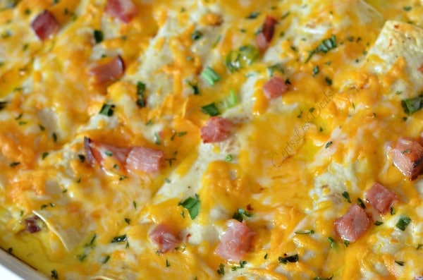 Breakfast enchiladas in a casserole dish topped with green onions, parsley and bits of ham