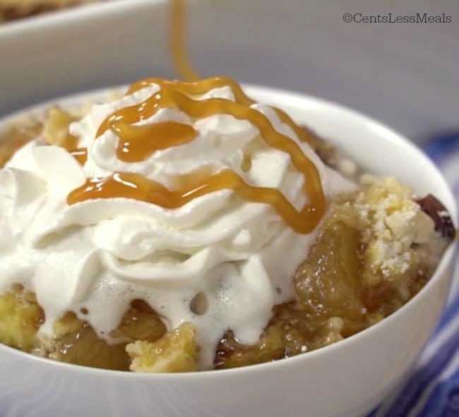 Caramel apple dump cake in a white bowl with whipped cream and caramel sauce on top