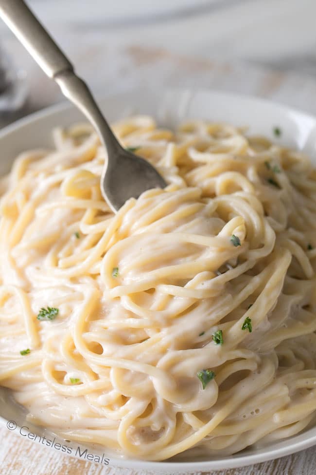 Pasta and copycat Olive Garden alfredo sauce in a bowl with a fork and parsley