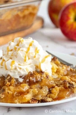 Caramel apple dump cake on a white plate with whipped cream on top