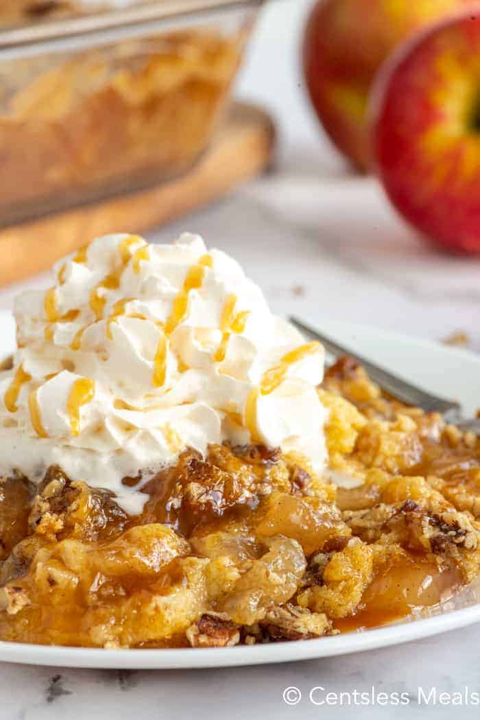 Caramel apple dump cake on a white plate with whipped cream on top