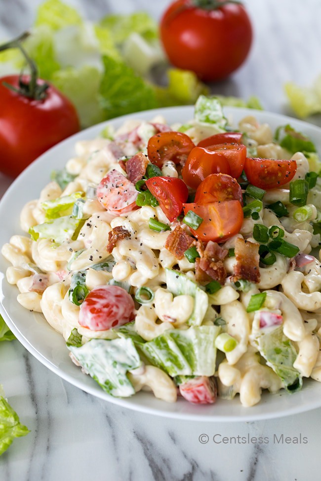 BLT pasta salad in a white bowl with bacon tomatoes and green onion as garnish