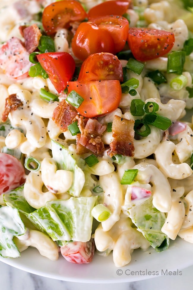 BLT pasta salad in a white bowl with tomatoes and green onion on top