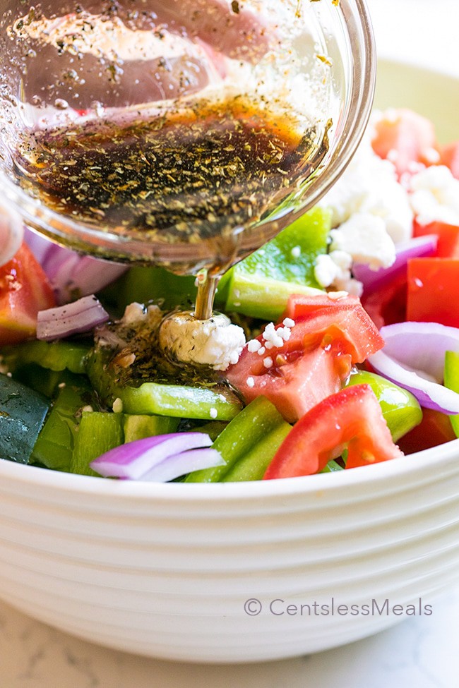 Easy Greek salad in a white bowl with dressing being poured on