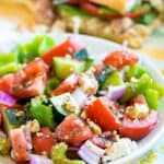 Easy Greek salad on a white plate with a Subway sandwich in the background