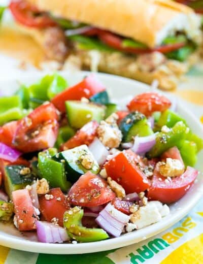 Easy Greek salad on a white plate with a Subway sandwich in the background