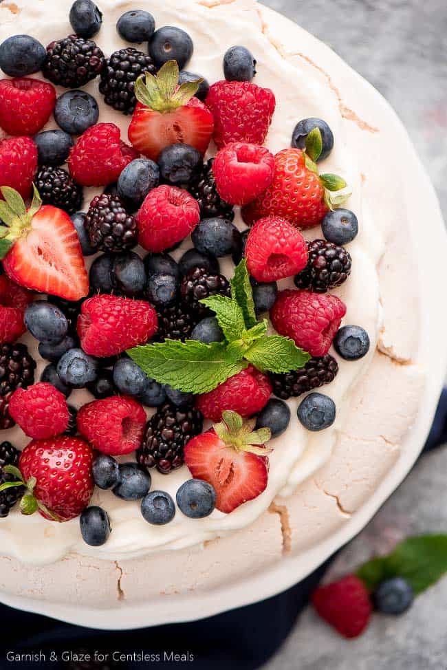 Berry topped Pavlova on a white plate with mint leaves as garnish