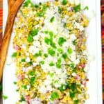 Mexican Corn Salad on a white serving plate with cilantro and a wooden spoon