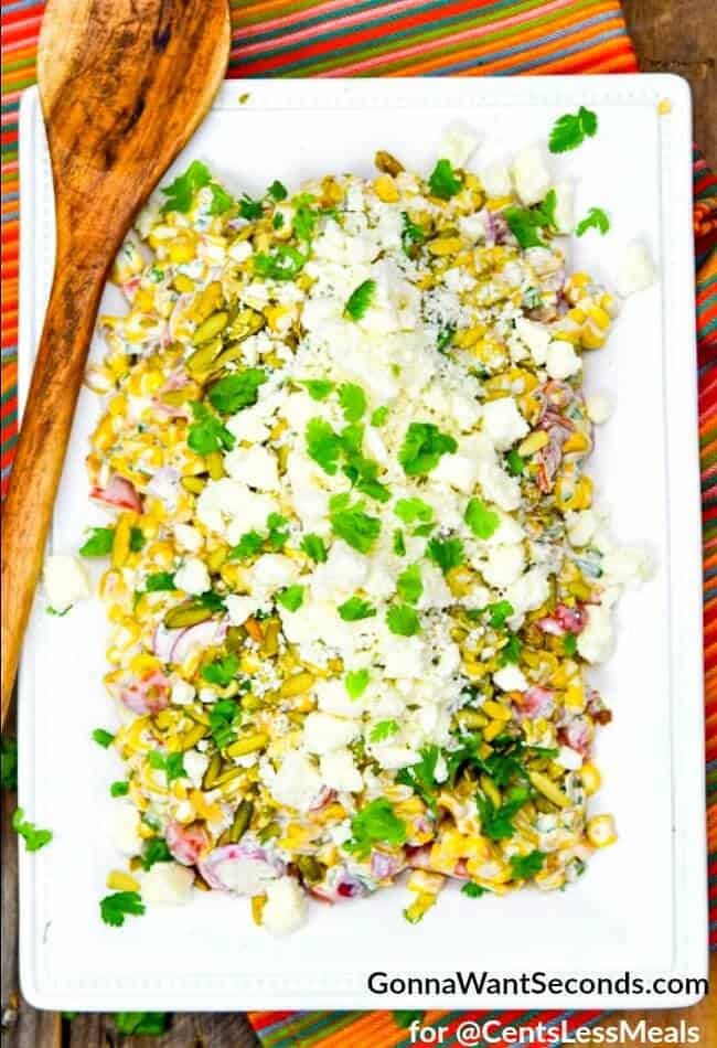 Mexican Corn Salad on a white serving plate with cilantro and a wooden spoon