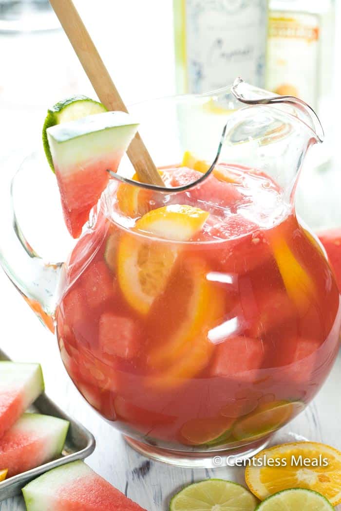 Watermelon sangria in a glass pitcher with watermelon lemon and lime slices