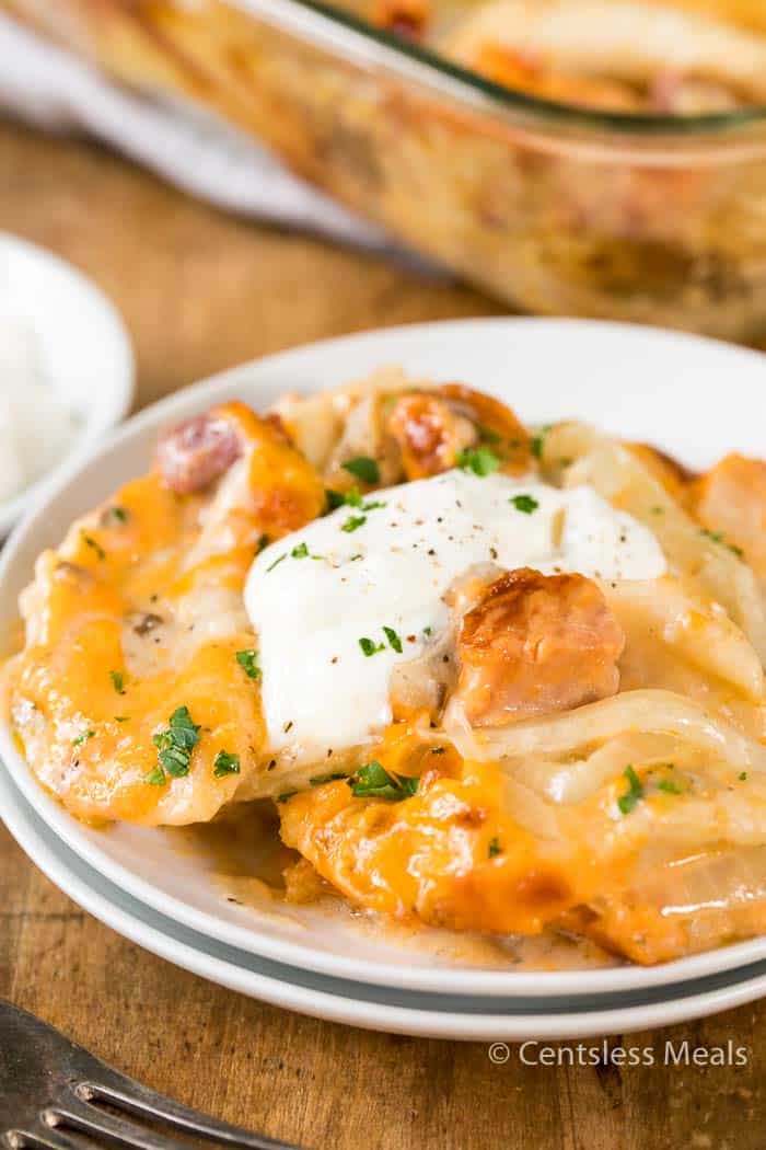 Pierogi casserole on a white plate with sour cream and parsley