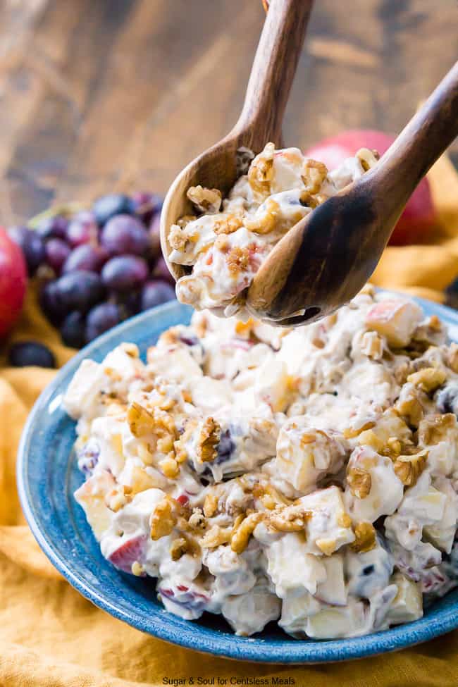 Apple walnut salad in a blue bowl with some being scooped up with wooden utensils