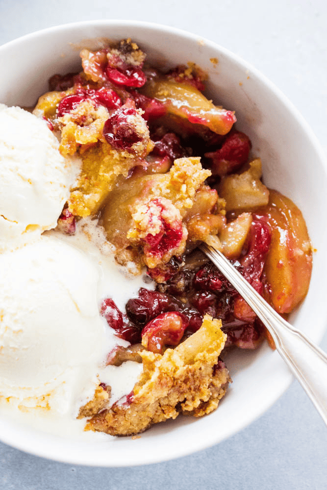 Apple cranberry crisp in a bowl with ice cream and a spoon