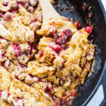 Apple cranberry crisp in a pan with a wooden spoon