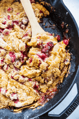 Apple cranberry crisp in a pan with a wooden spoon