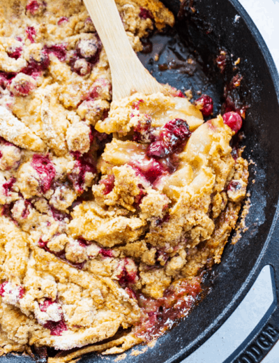 Apple cranberry crisp in a pan with a wooden spoon