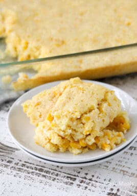 Creamed corn casserole on a white plate with the casserole dish on the side