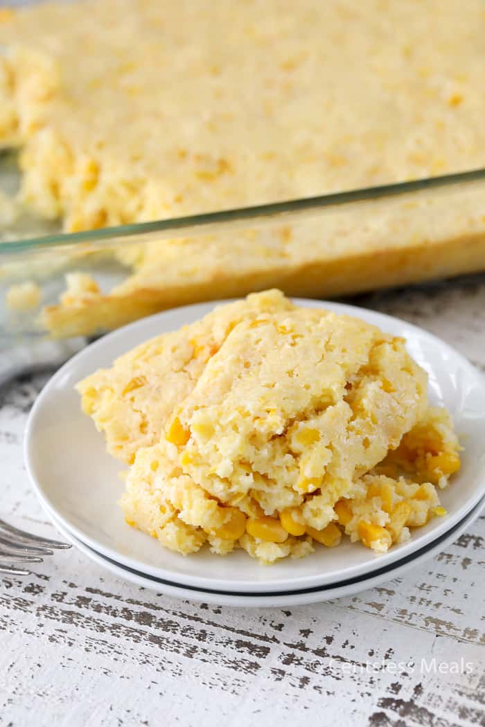 Creamed corn casserole on a white plate with the casserole dish on the side