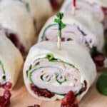 Cranberry turkey pinwheels on a wooden board with cranberries on the side