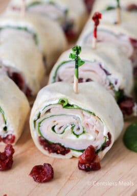 Cranberry turkey pinwheels on a wooden board with cranberries on the side