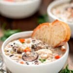 Slow cooker chicken wild rice soup in a white bowl with a slice of bread and a spoon on the side