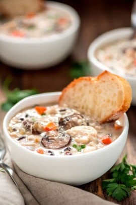 Slow cooker chicken wild rice soup in a white bowl with a slice of bread and a spoon on the side