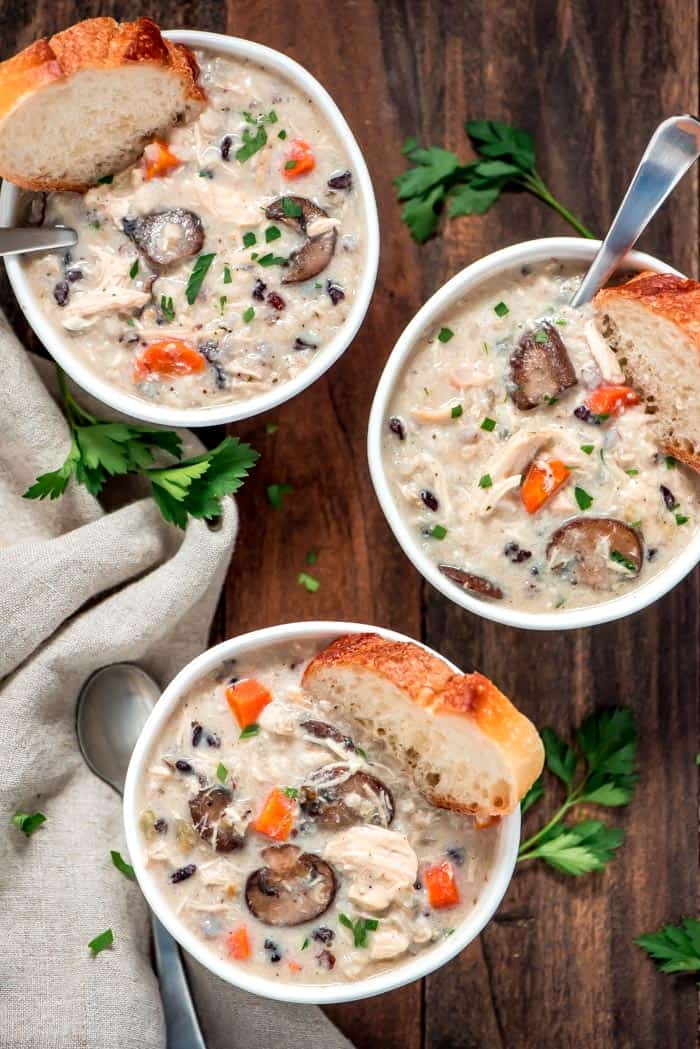 Three bowls of chicken wild rice soup with pieces of bread and spoons