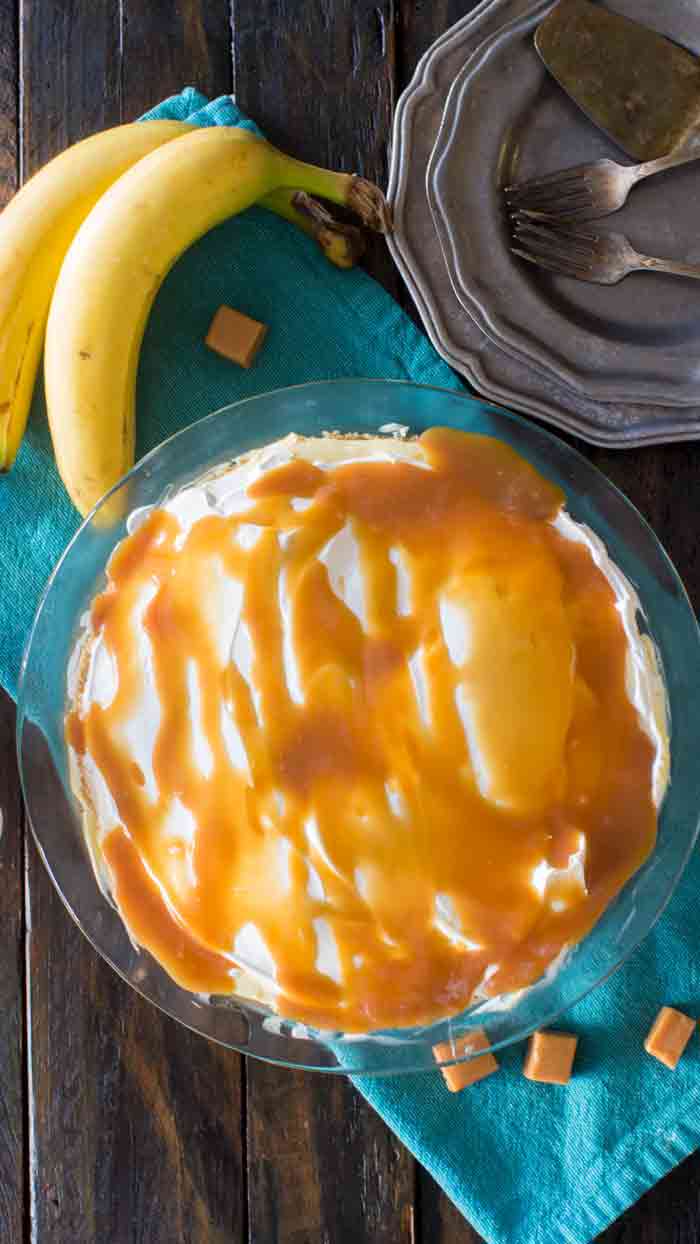 Salted caramel banana cream pie in a pie plate with plates and forks on the side