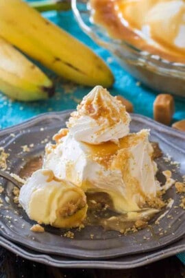 Piece of salted caramel banana cream pie on a plate with bananas in the background