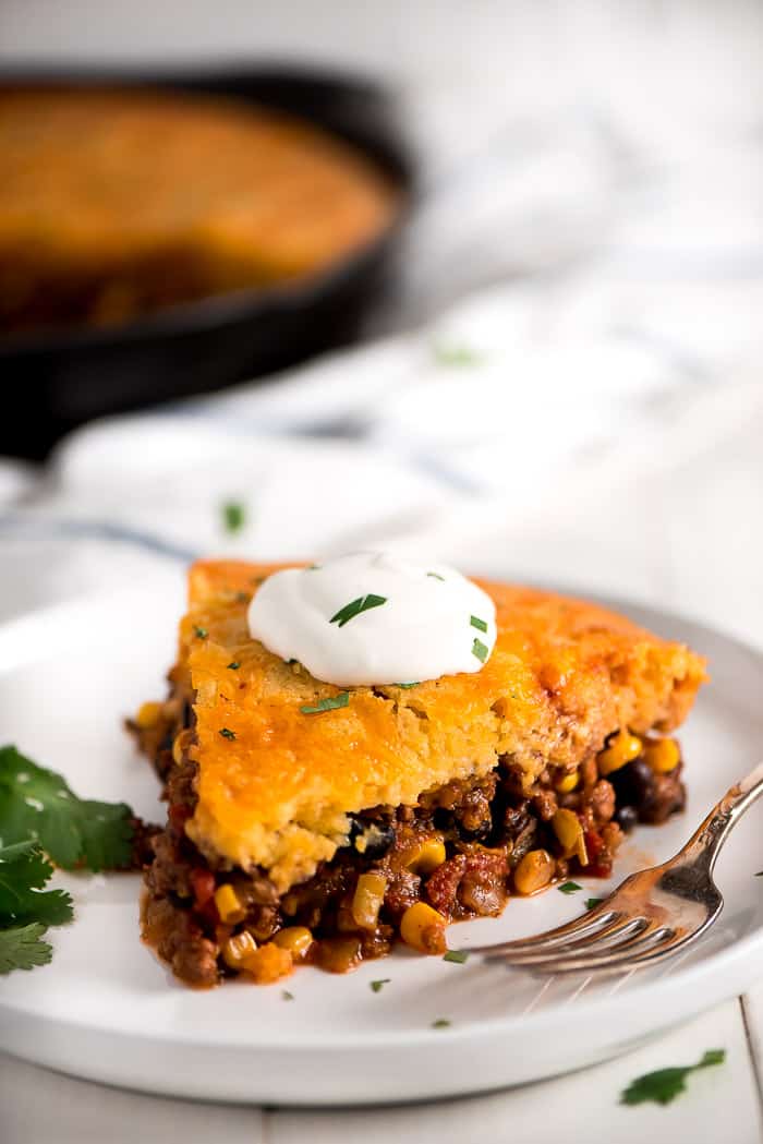 Piece of tamale pie on a white plate with a fork and a dollop of sour cream