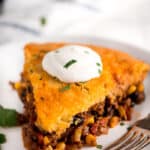 Tamale pie on a white plate with sour cream and a fork