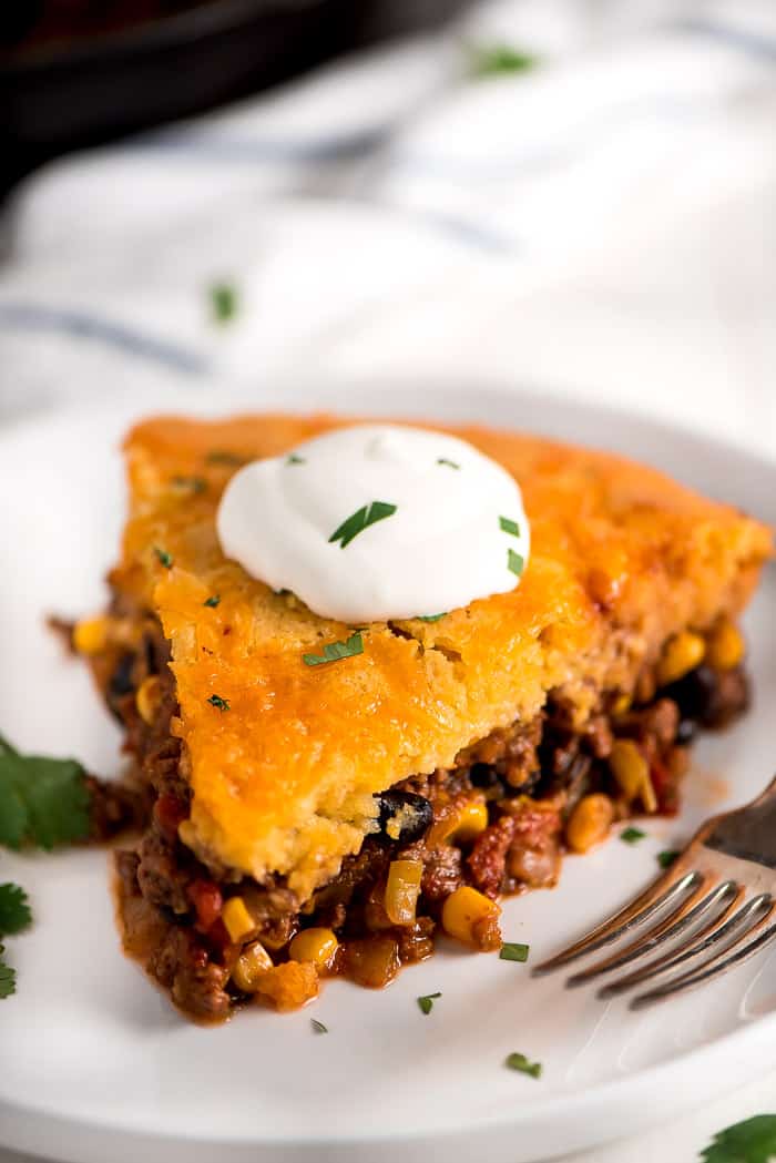 Tamale pie on a white plate with sour cream and a fork