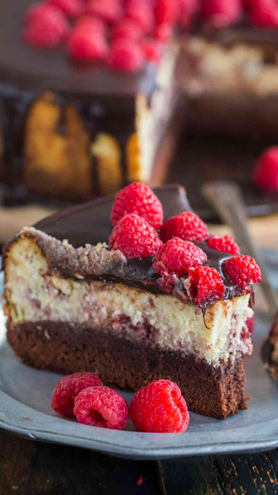 Brownie Bottom Raspberry Cheesecake served on a plate with a few raspberries on the side