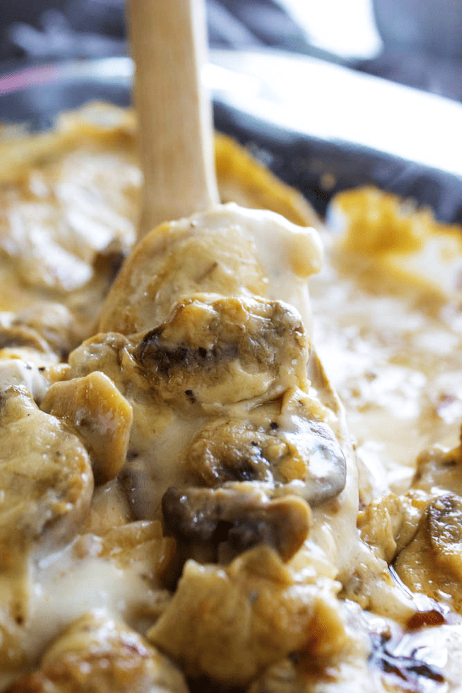 Using a wooden spoon to remove a serving of Chicken and Mushroom Casserole from baking dish