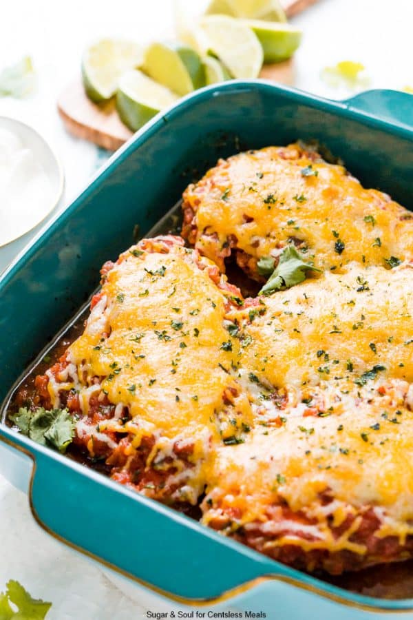 Four pieces of chicken in a teal baking dish with melted cheese on top