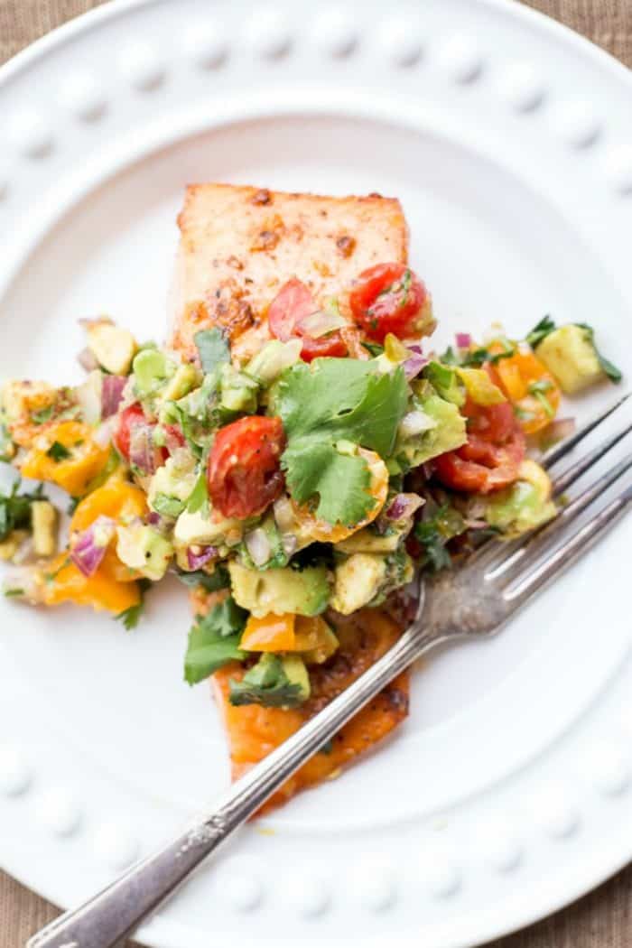 Baked salmon with avocado salsa on a white plate