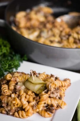 Cheeseburger pasta casserole on a white plate with a pickle on top