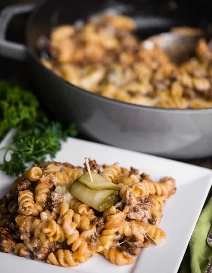 Cheeseburger pasta casserole on a white plate with a pickle on top
