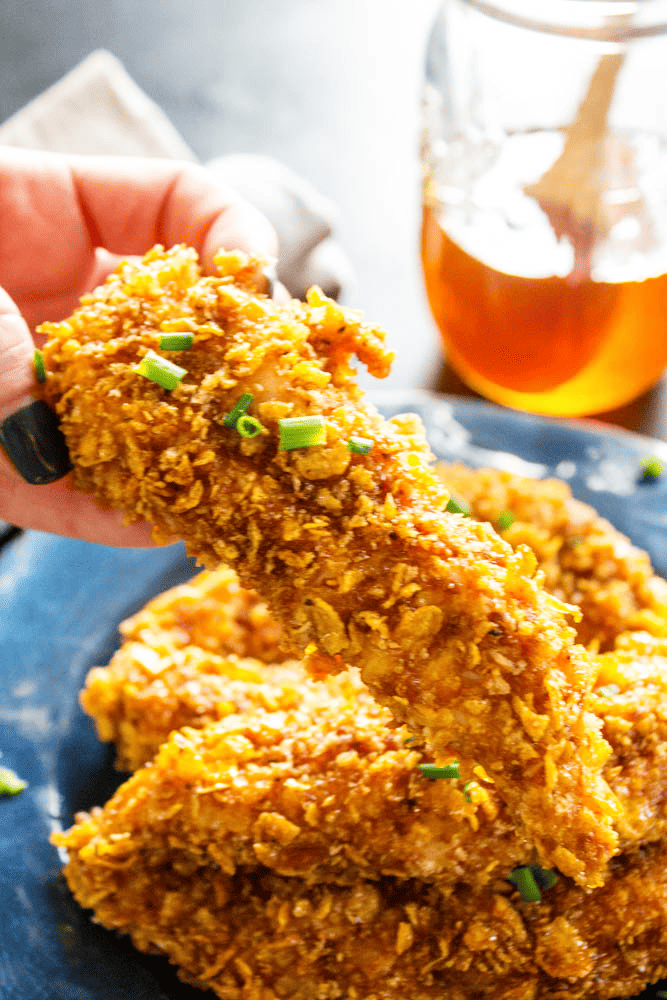 Baked honey garlic chicken tenders on a plate with one being held