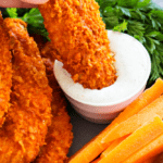 Baked buffalo chicken tenders being dipped in dip