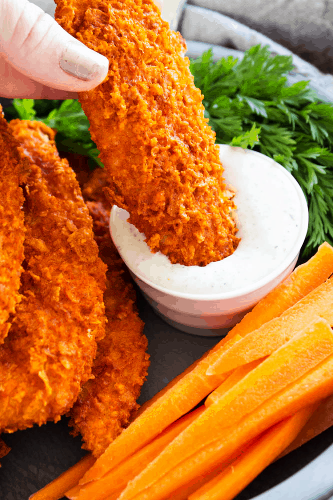 Baked buffalo chicken tenders being dipped in dip